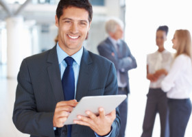 Portrait of smiling young business man working on digital tablet with executives in background